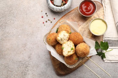 Photo of Delicious fried croquette balls with parsley, sauces and spices on grey textured table, flat lay. Space for text