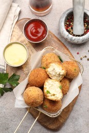 Photo of Delicious fried croquette balls with parsley, sauces and spices on grey textured table, flat lay