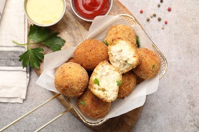 Photo of Delicious fried croquette balls with parsley, sauces and spices on grey textured table, flat lay