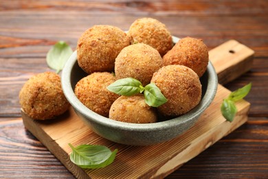 Photo of Delicious fried croquette balls with basil in bowl on wooden table, closeup
