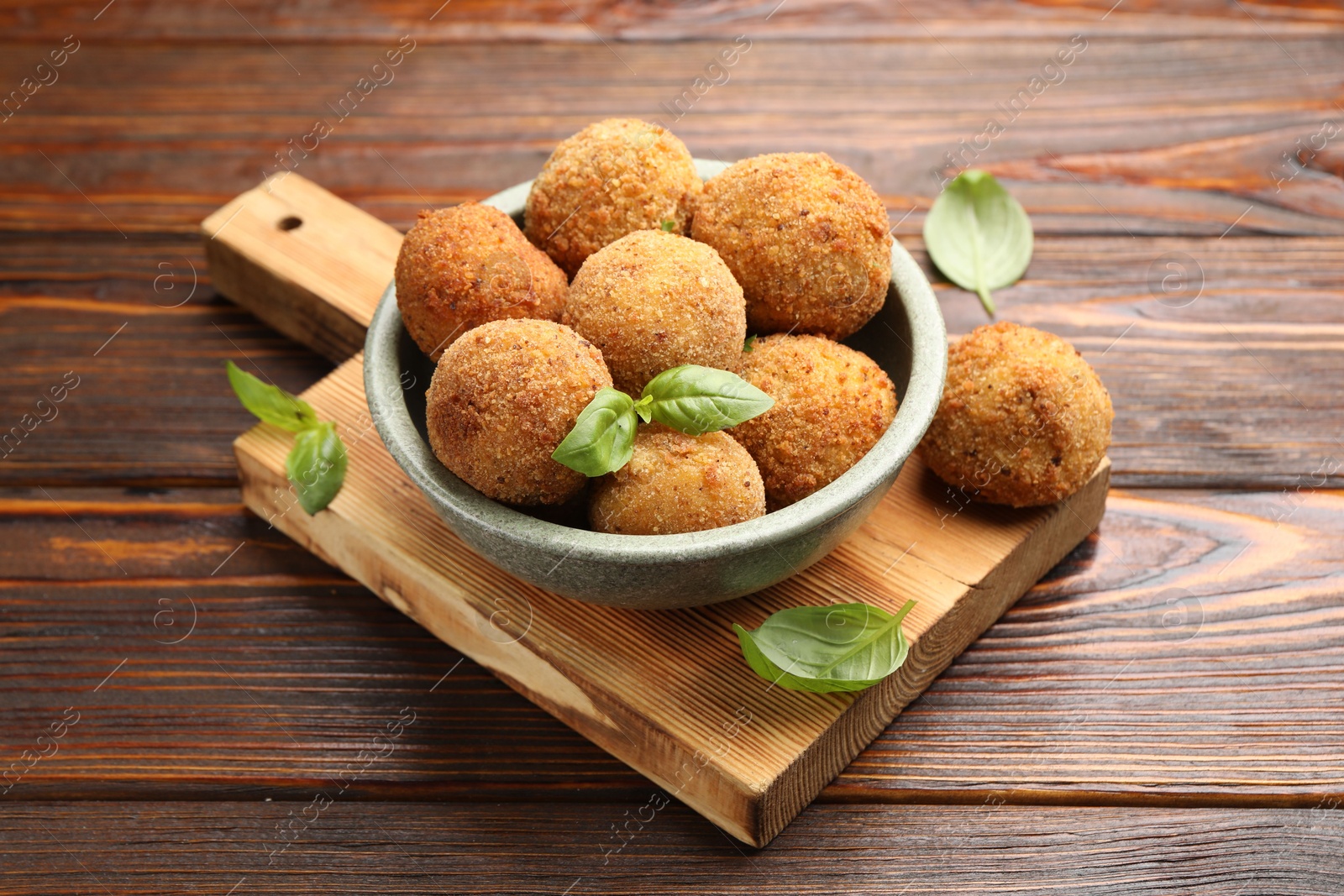 Photo of Delicious fried croquette balls with basil in bowl on wooden table, closeup