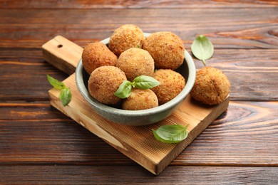 Photo of Delicious fried croquette balls with basil in bowl on wooden table, closeup