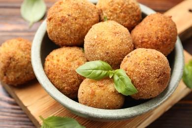 Photo of Delicious fried croquette balls with basil in bowl on wooden table, closeup