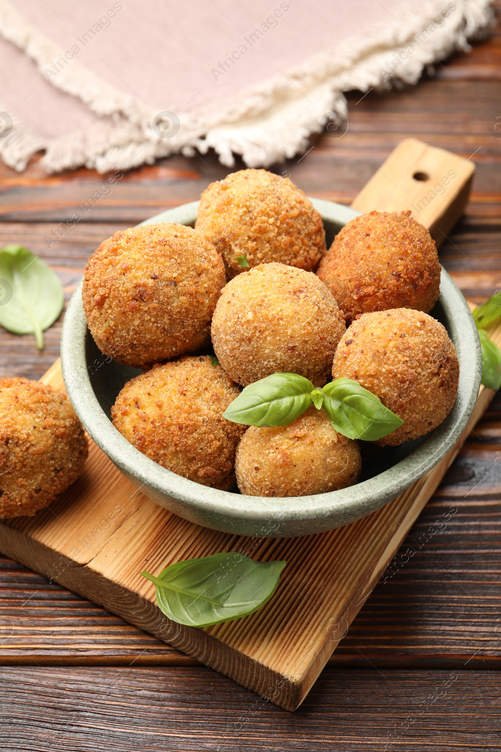 Photo of Delicious fried croquette balls with basil in bowl on wooden table, closeup