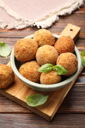 Photo of Delicious fried croquette balls with basil in bowl on wooden table, closeup
