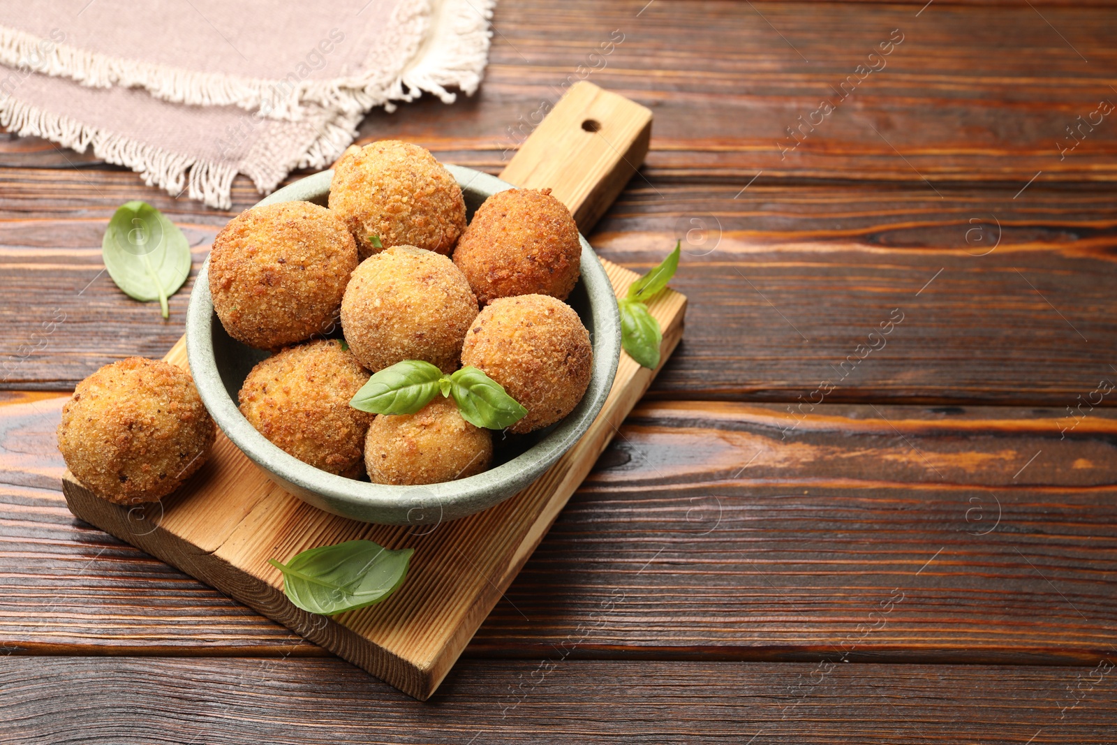 Photo of Delicious fried croquette balls with basil in bowl on wooden table, closeup