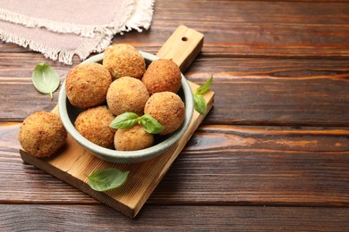 Photo of Delicious fried croquette balls with basil in bowl on wooden table, closeup