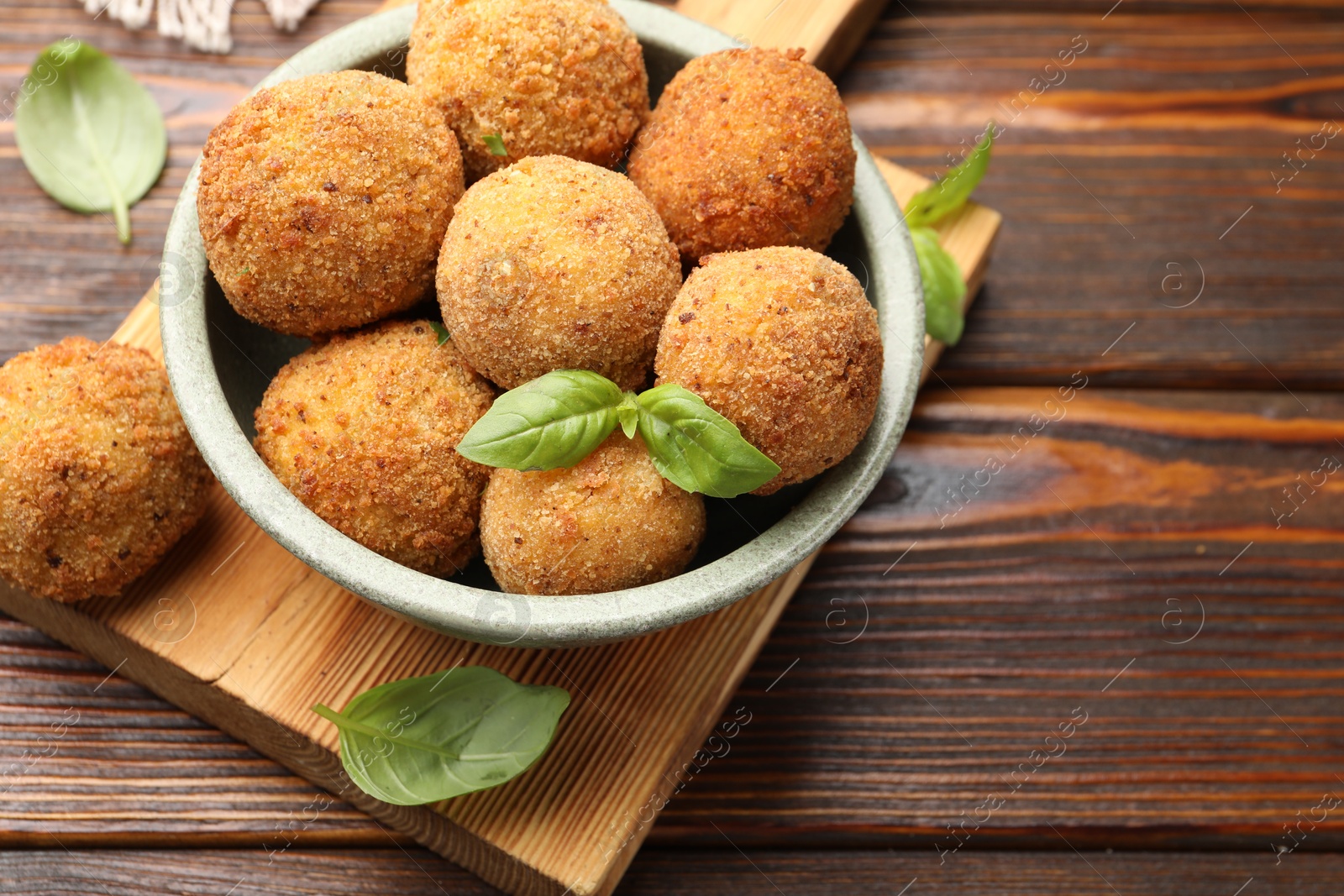Photo of Delicious fried croquette balls with basil in bowl on wooden table, closeup