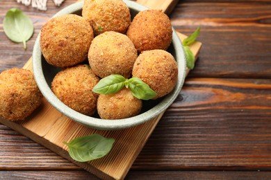 Photo of Delicious fried croquette balls with basil in bowl on wooden table, closeup