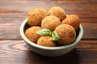 Photo of Delicious fried croquette balls with basil in bowl on wooden table, closeup