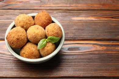 Photo of Delicious fried croquette balls with basil in bowl on wooden table, closeup. Space for text