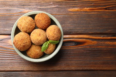 Photo of Delicious fried croquette balls with basil in bowl on wooden table, top view. Space for text
