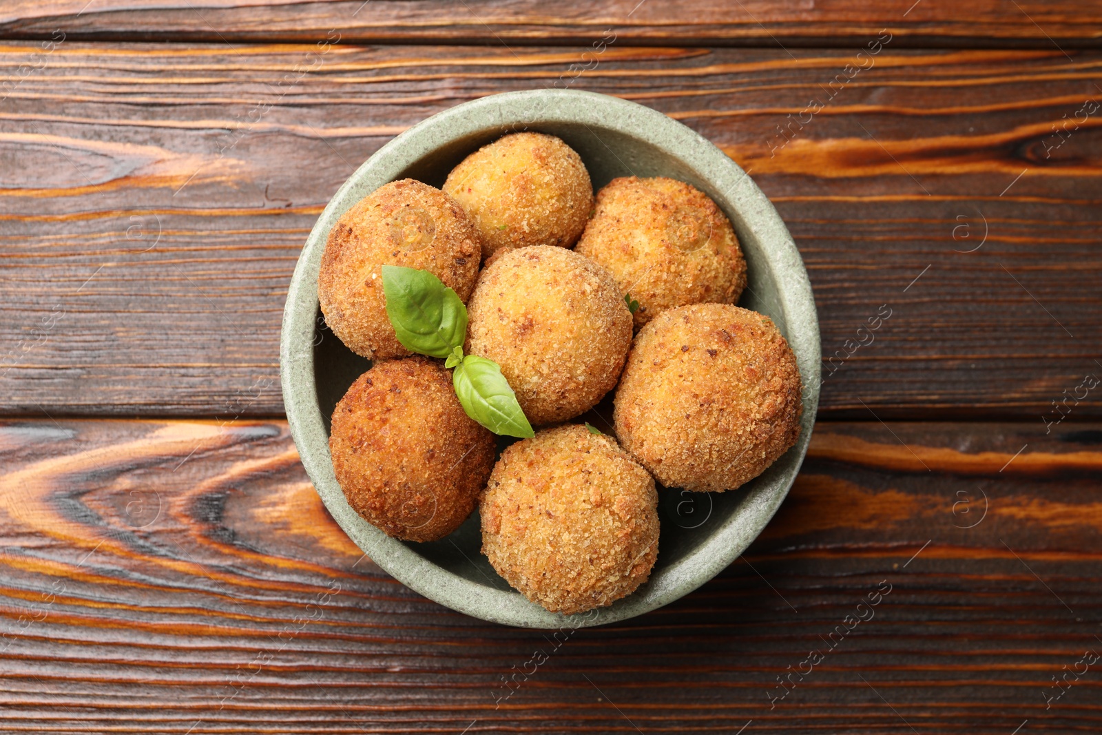 Delicious fried croquette balls with basil in bowl on wooden table, top view Photo of Delicious fried croquette balls with basil in bowl on wooden table, top view