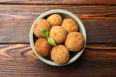 Photo of Delicious fried croquette balls with basil in bowl on wooden table, top view