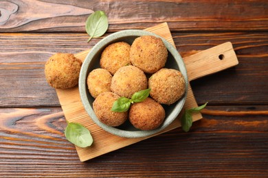 Photo of Delicious fried croquette balls with basil in bowl on wooden table, flat lay
