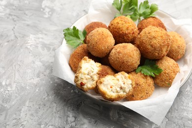Photo of Delicious fried croquette balls with parsley in bowl on grey textured table, closeup. Space for text
