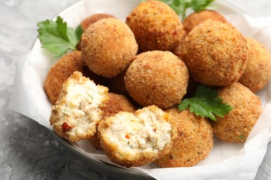 Photo of Delicious fried croquette balls with parsley in bowl on grey textured table, closeup