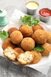 Photo of Delicious fried croquette balls with parsley in bowl on grey textured table, closeup