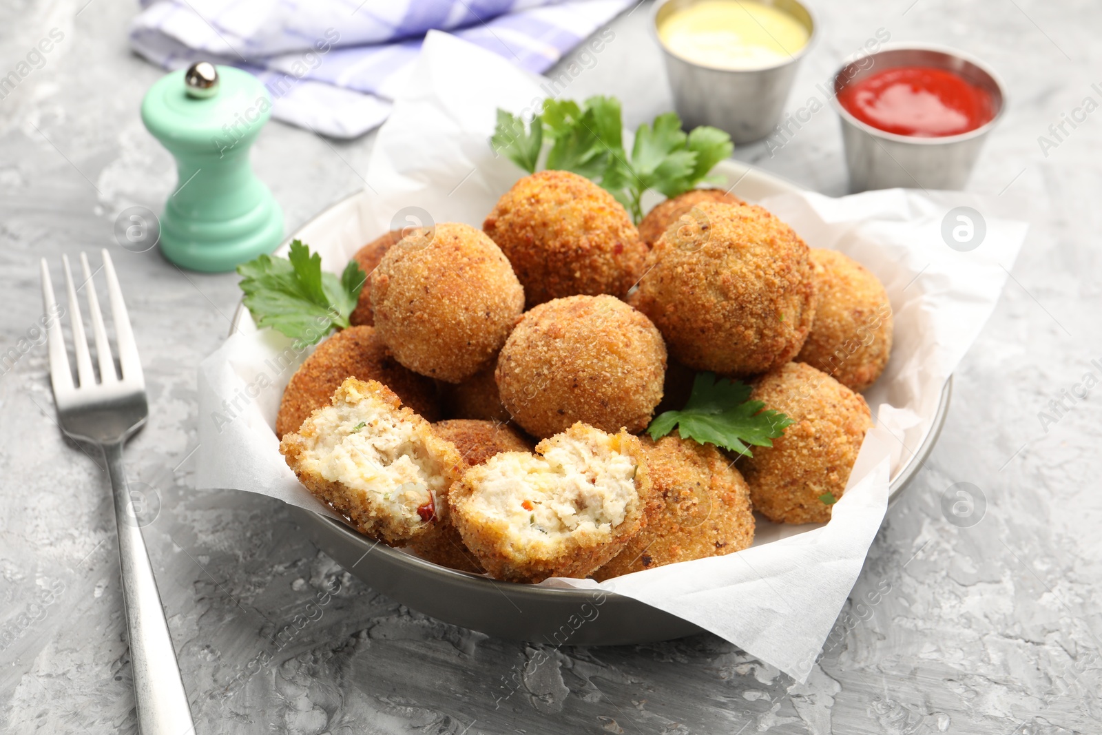 Photo of Delicious fried croquette balls with parsley in bowl and fork on grey textured table, closeup
