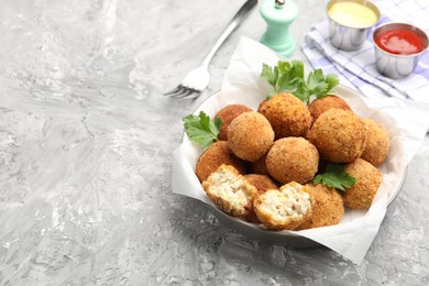 Photo of Delicious fried croquette balls with parsley in bowl on grey textured table, closeup. Space for text