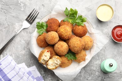 Photo of Delicious fried croquette balls with parsley and sauces served on grey textured table, flat lay