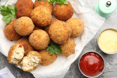 Photo of Delicious fried croquette balls with parsley and sauces on grey textured table, flat lay