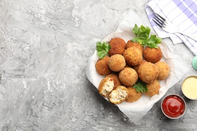 Photo of Delicious fried croquette balls with parsley and sauces on grey textured table, flat lay. Space for text