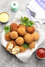 Photo of Delicious fried croquette balls with parsley and sauces served on grey textured table, flat lay