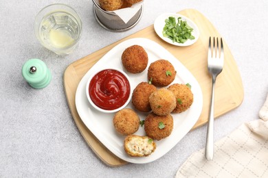 Photo of Delicious fried croquette balls with parsley and ketchup served on grey textured table, flat lay