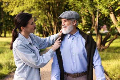 Photo of Smiling caregiver supporting elderly man in park