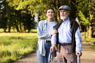 Photo of Smiling caregiver supporting elderly man who using walking frame outdoors. Space for text
