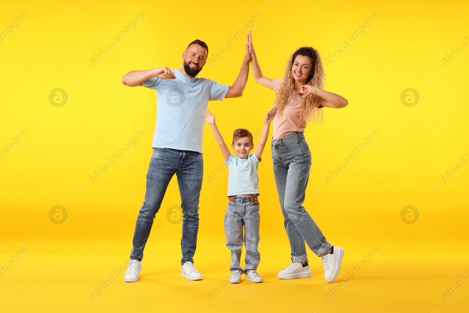 Happy family. Parents giving high five and their son on yellow background Photo of Happy family. Parents giving high five and their son on yellow background