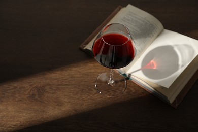 Photo of Glass of wine and book on wooden table. Space for text