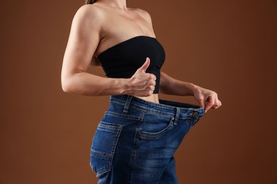 Photo of Fit woman wearing old jeans after weight loss and showing thumbs up on brown background, closeup
