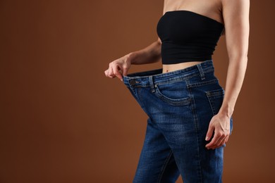 Photo of Fit woman wearing old jeans after weight loss on brown background, closeup. Space for text