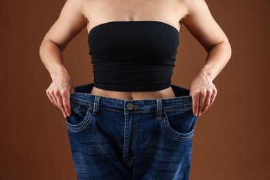 Photo of Fit woman wearing old jeans after weight loss on brown background, closeup