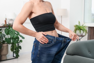 Photo of Fit woman wearing old jeans after weight loss at home, closeup