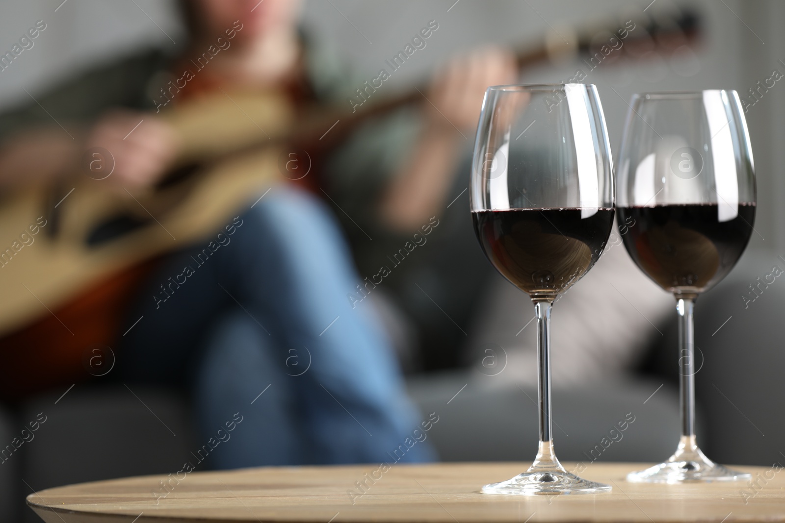 Glasses with red wine on table and man playing guitar indoors, selective focus Photo of Glasses with red wine on table and man playing guitar indoors, selective focus