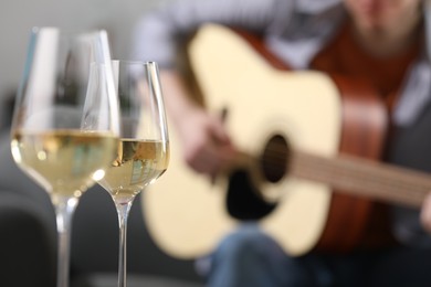 Photo of Glasses with white wine and man playing guitar indoors, selective focus