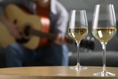 Photo of Glasses with white wine on table and man playing guitar indoors, selective focus