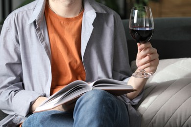 Photo of Woman with glass of wine reading book on sofa at home, closeup