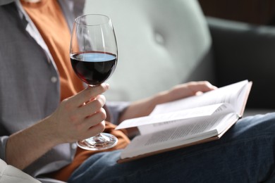 Photo of Woman with glass of wine reading book on sofa at home, closeup