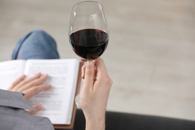 Photo of Woman with glass of wine reading book on sofa at home, closeup. Space for text