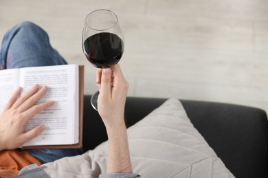 Photo of Woman with glass of wine reading book on sofa at home, closeup. Space for text