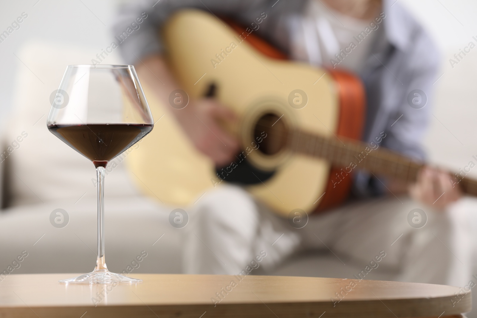 Glass with red wine on table and man playing guitar indoors, selective focus Photo of Glass with red wine on table and man playing guitar indoors, selective focus