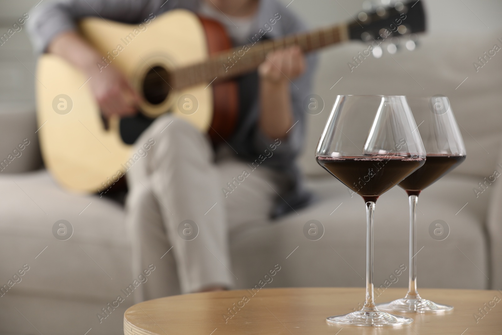 Glasses with red wine on table and man playing guitar indoors, selective focus Photo of Glasses with red wine on table and man playing guitar indoors, selective focus
