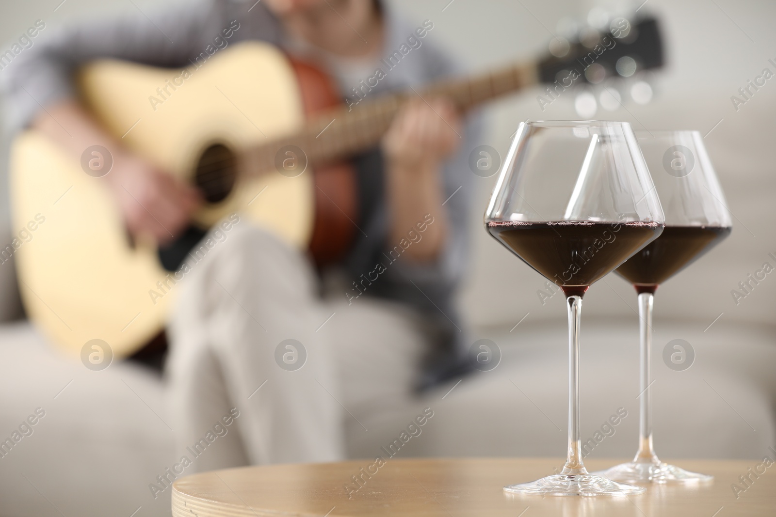 Glasses with red wine on table and man playing guitar indoors, selective focus Photo of Glasses with red wine on table and man playing guitar indoors, selective focus