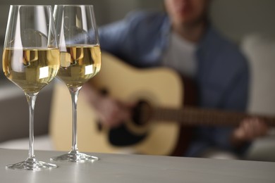 Photo of Glasses with white wine on table and man playing guitar indoors, selective focus