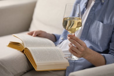 Photo of Woman with glass of wine reading book on sofa at home, closeup
