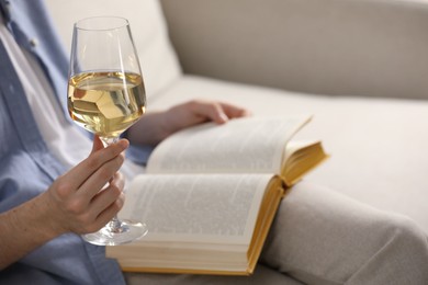 Photo of Woman with glass of wine reading book on sofa at home, closeup